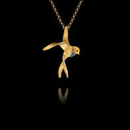 Sterling silver swallow pendant with gold-plated body and rhodium-plated accent, showing the bird with outstretched wings in a mid-flight pose, hanging on a gold chain against a black background.