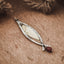 Long fish pendant with an engraved hatched silver outer frame, gold-plated brass inner body and forked tail with a red coral bead drop, displayed on a wooden surface.