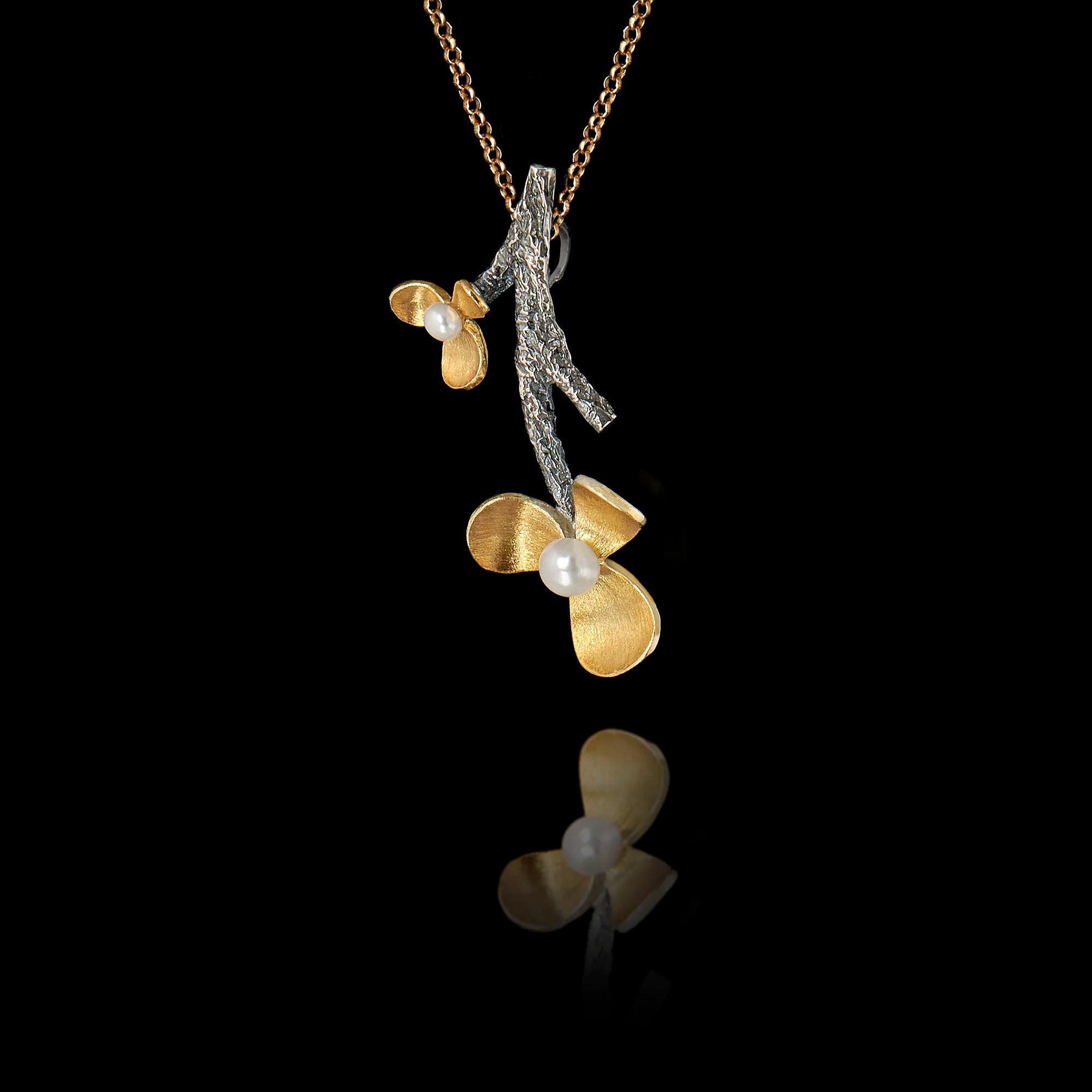 Side angle view of a 925 sterling silver flower branch pendant showing the textured oxidised branch and gold-plated floral blooms with freshwater pearl centres on a gold chain against a black background.