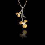 925 sterling silver flower branch pendant with oxidised silver forked branch and two gold-plated three-petal blooms each centred with a freshwater pearl, on a gold chain against a black background.