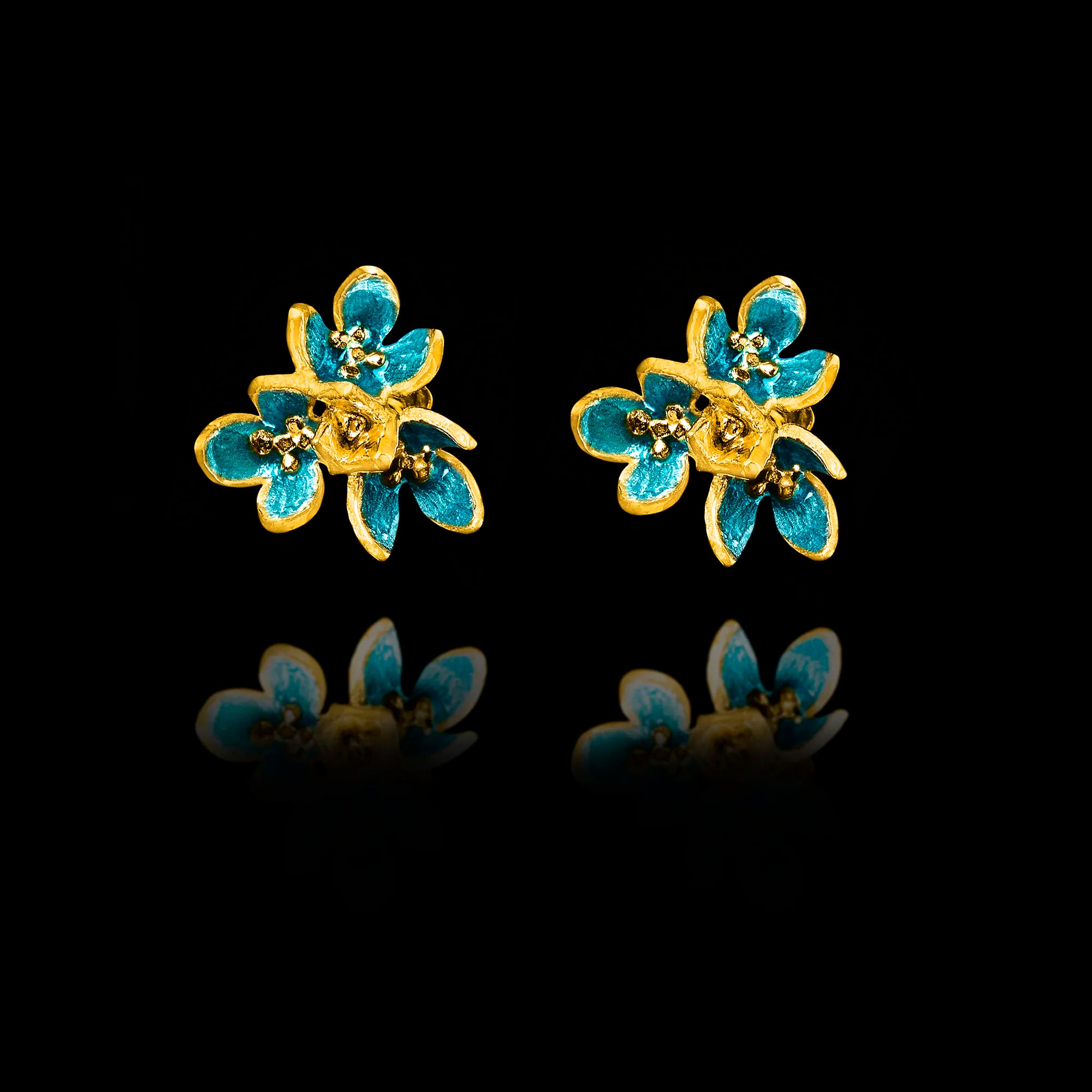 Front view of gold flower stud earrings with layered petals and vibrant turquoise enamel detailing.