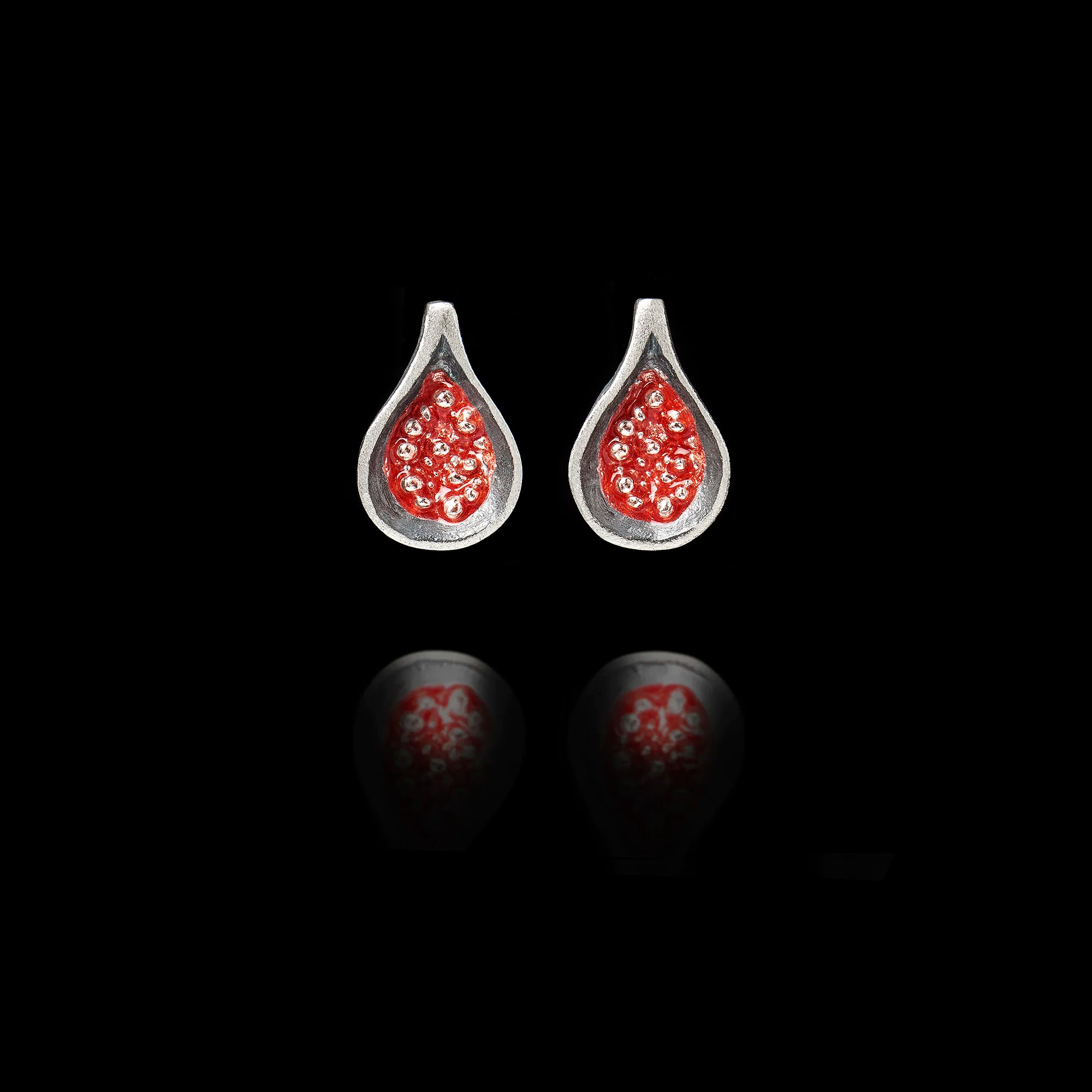Front view of silver fig stud earrings with a dark oxidized exterior and a vibrant red enamel seed cluster in the center. Main image