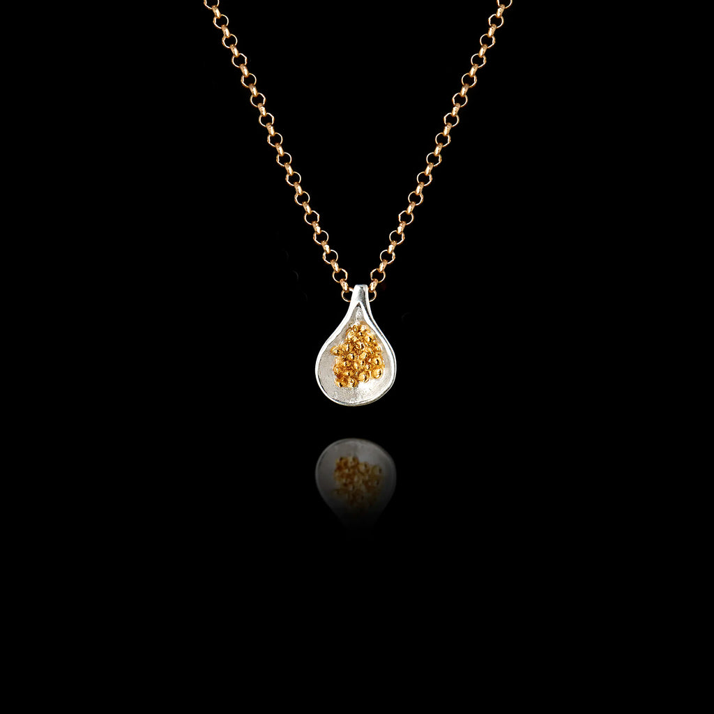 925 sterling silver fig pendant with rhodium-plated teardrop frame and cluster of gold-plated granule seeds inside, hanging on a gold chain against a black background.
