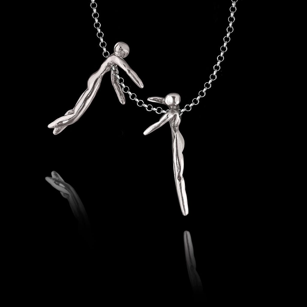 Detail view of a handcrafted 925 sterling silver hug pendant showing the two abstract human figures separated on the chain, each reaching towards the other, against a black background.