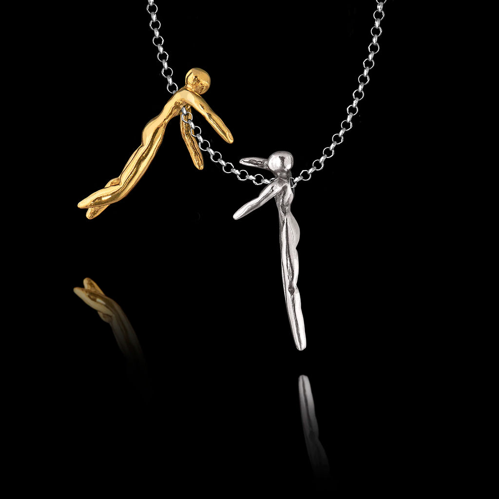 Detail view of a handcrafted 925 sterling silver hug pendant showing a silver and a gold-plated figures separated on the chain, each reaching towards the other, against a black background.