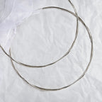 Full view of handmade sterling silver Stefana with triple round wire and white ribbon on a textured background.