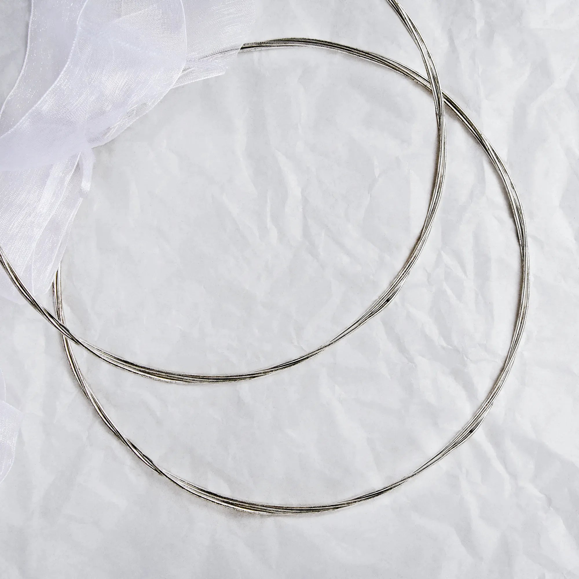 Full view of handmade sterling silver Stefana with triple round wire and white ribbon on a textured background.