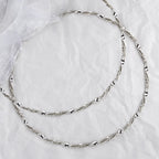 Full view of handmade 925 sterling silver Stefana with a dynamic twisted ribbon and wire design on a white textured background.