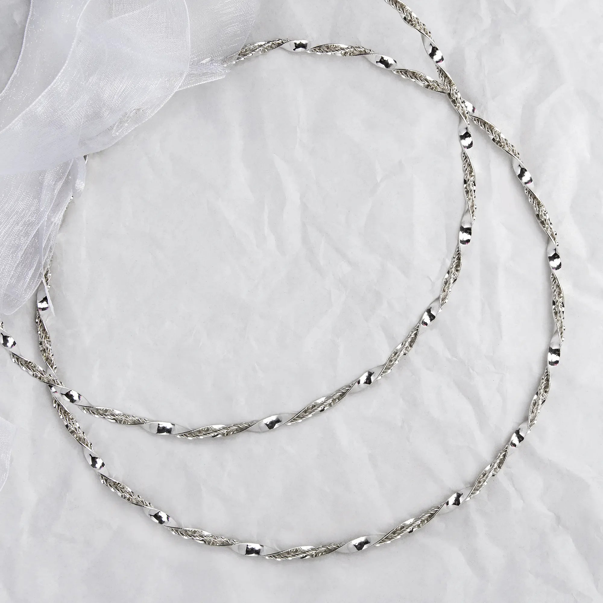 Full view of handmade 925 sterling silver Stefana with a dynamic twisted ribbon and wire design on a white textured background. Main image