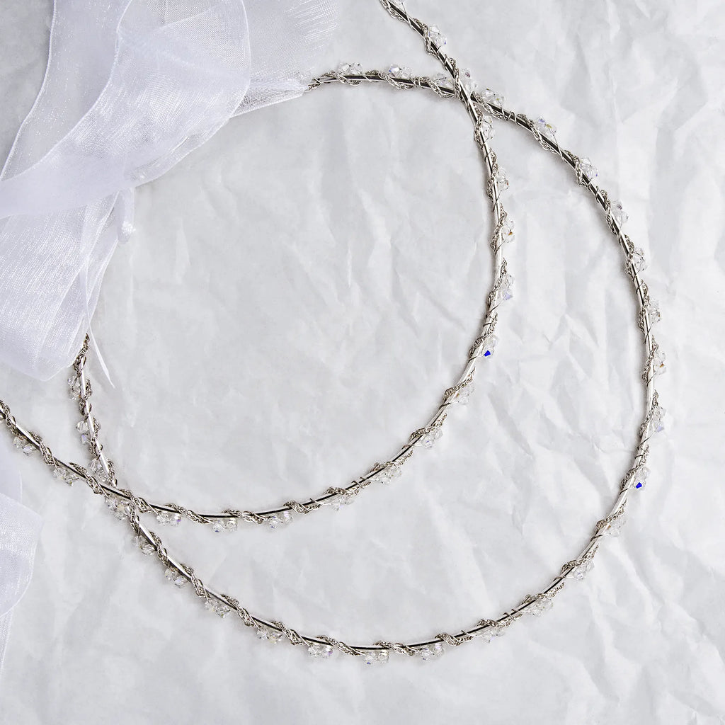 Handmade sterling silver wedding crowns with Spiga chain and Swarovski crystals on white textured background with ribbon.