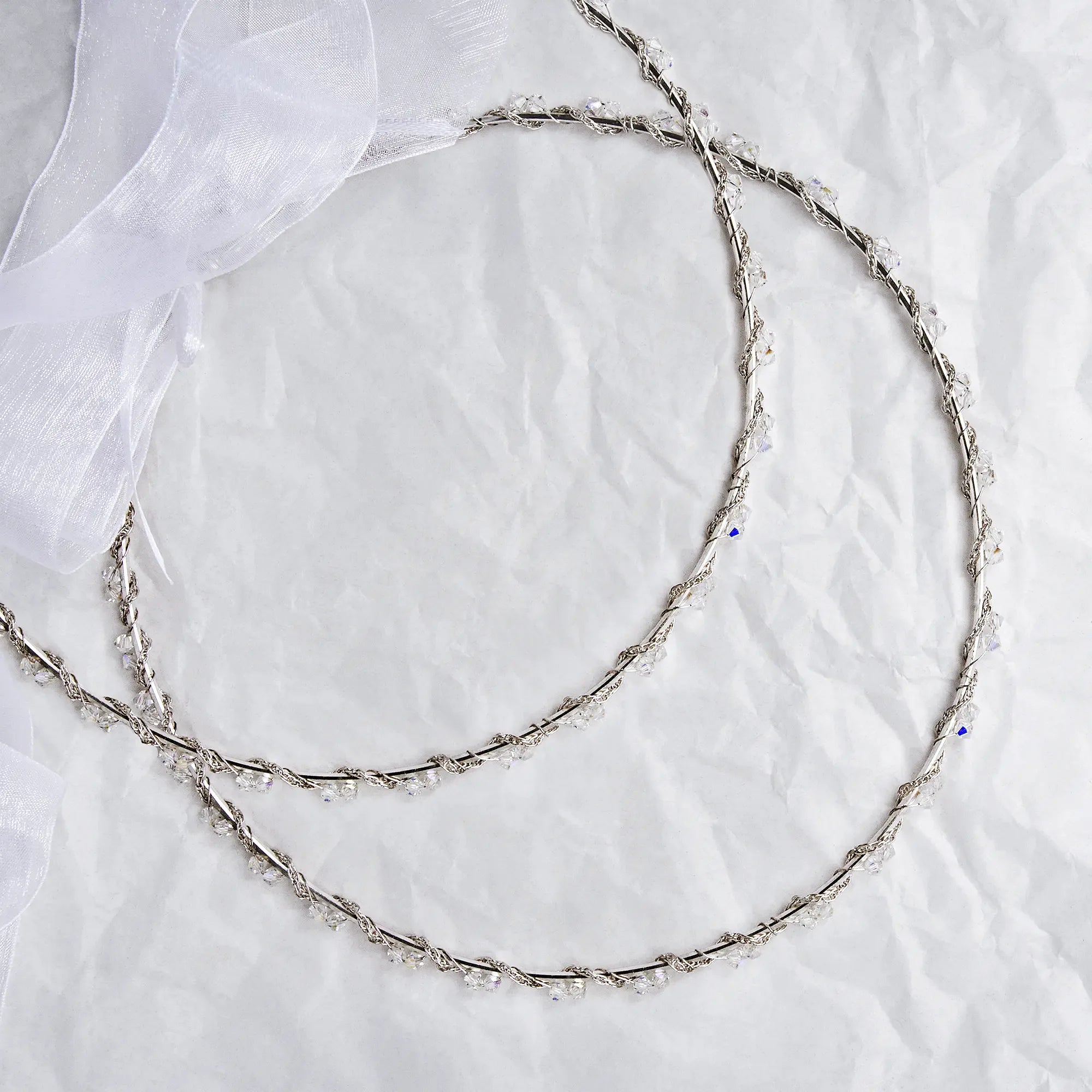 Handmade sterling silver wedding crowns with Spiga chain and Swarovski crystals on white textured background with ribbon.