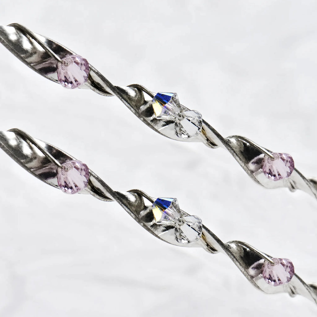 Close-up of twisted sterling silver ribbon wedding crowns featuring sparkling pink and white Swarovski crystals.