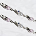 Close-up of twisted sterling silver ribbon wedding crowns featuring sparkling pink and white Swarovski crystals.