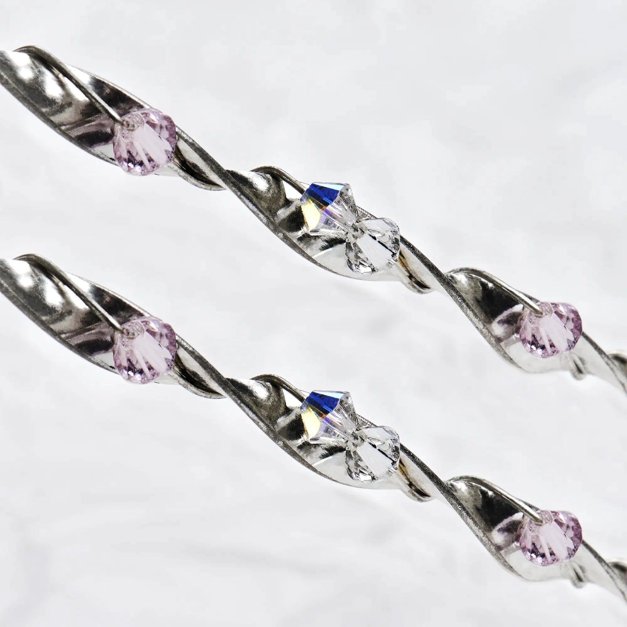Close-up of twisted sterling silver ribbon wedding crowns featuring sparkling pink and white Swarovski crystals.