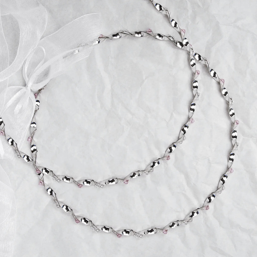 Full view of handmade sterling silver wedding crowns with pink crystals and white ribbon on a white textured background.