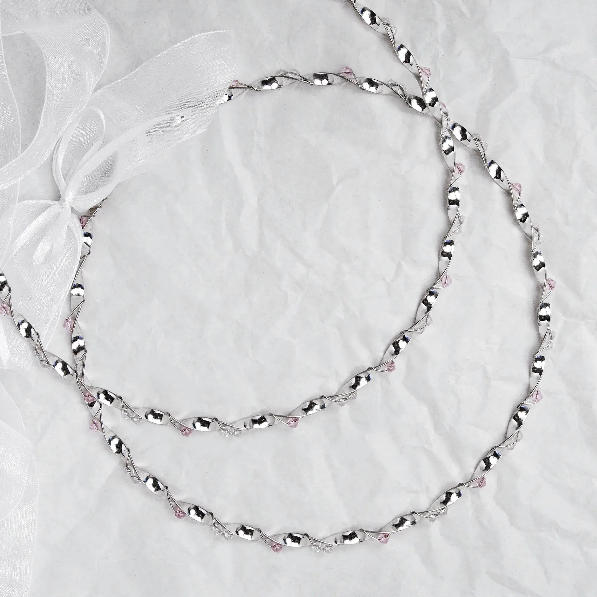 Full view of handmade sterling silver wedding crowns with pink crystals and white ribbon on a white textured background. Main image