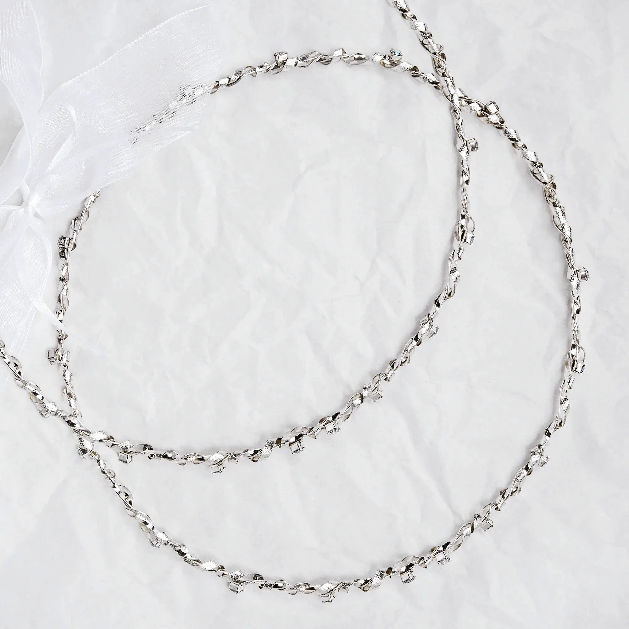 Full view of handmade sterling silver wedding crowns with a twisted base, hammered ribbon, and colorful crystals on a textured background. Main image