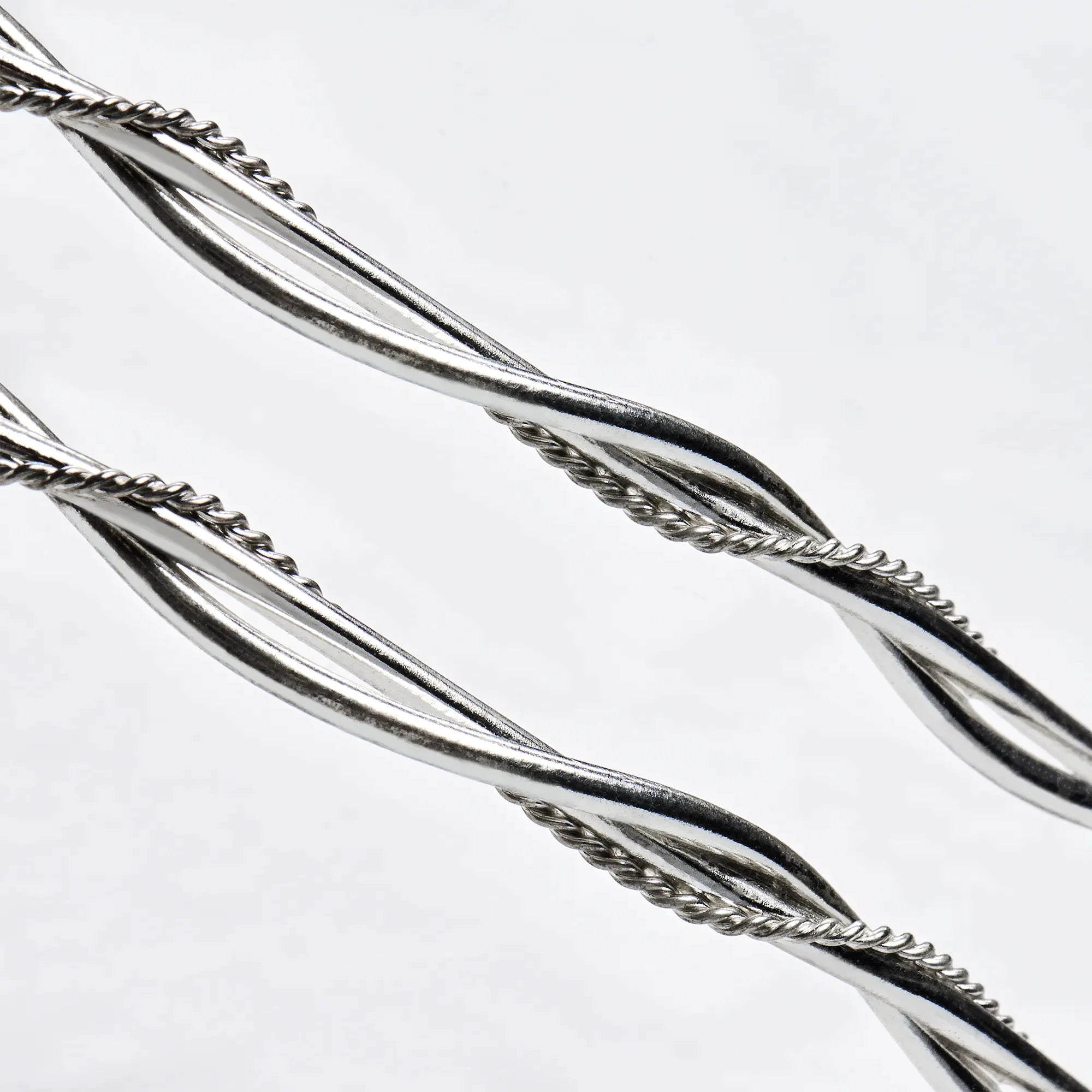 Close-up detail of two thick round sterling silver wires braided together with a delicate twisted wire.