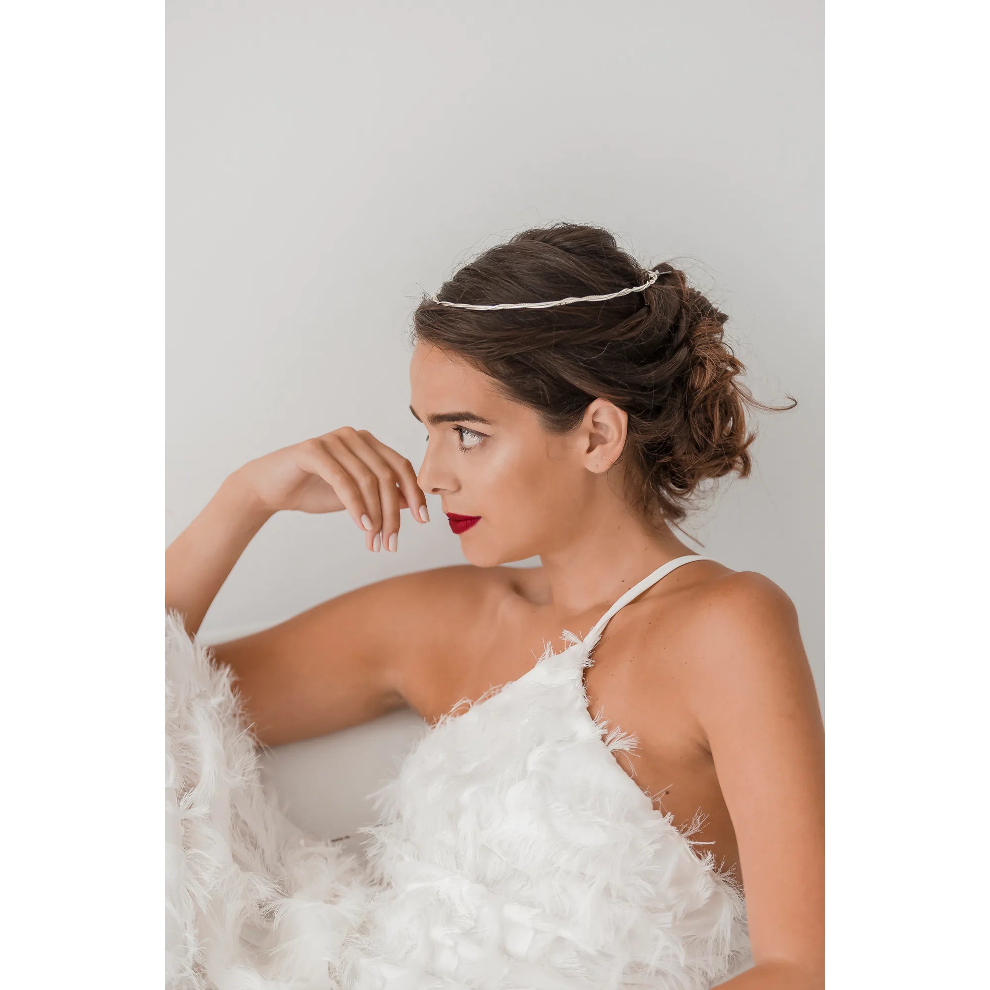 Woman in a white dress with feathered details and a wedding crown against a plain background