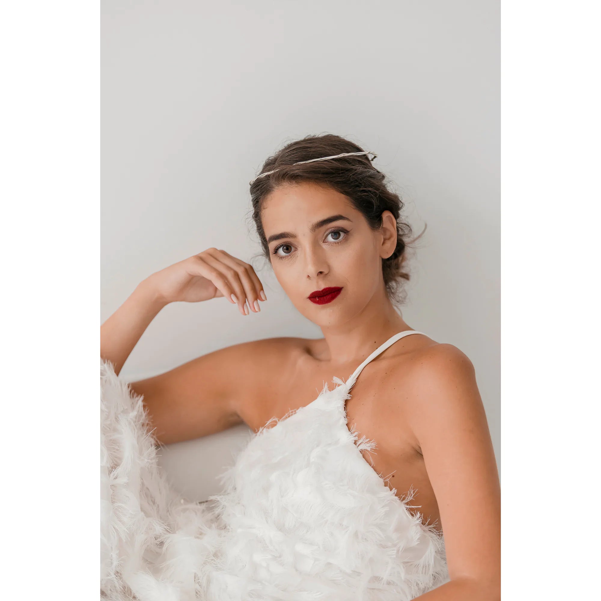 Woman in a white lace dress with a wedding crown  and red lipstick against a plain background