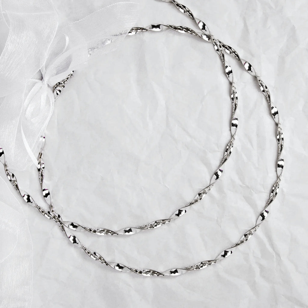 Full view of handmade twisted sterling silver wedding crowns with a white ribbon on a textured background.