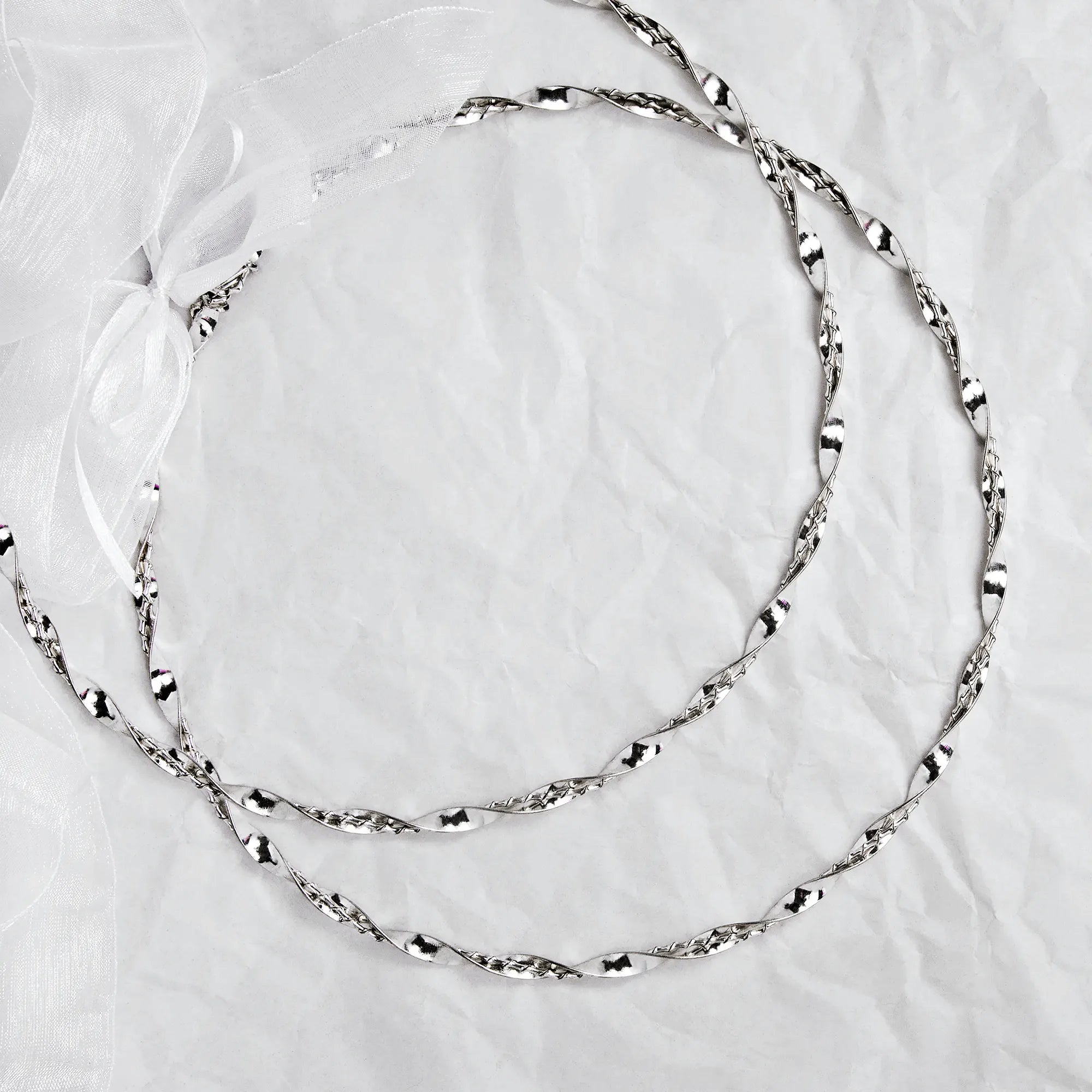 Full view of handmade twisted sterling silver wedding crowns with a white ribbon on a textured background. Main image